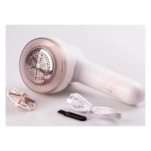 White handheld fabric shaver with a round metal mesh head, shown with its power cord and extra blade attachments on a white surface.