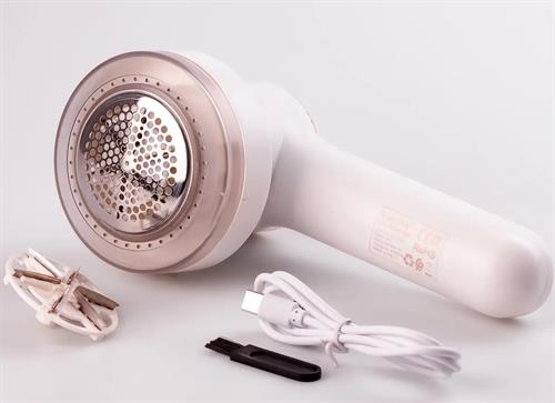 CSYSK12005W - Computech-Solutions White handheld fabric shaver with a round metal mesh head, shown with its power cord and extra blade attachments on a white surface.