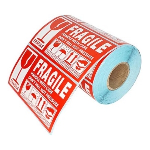 Roll of red 'Fragile' handling labels with 'Handle with care' text and icons, wound around a blue parcel-label roll.